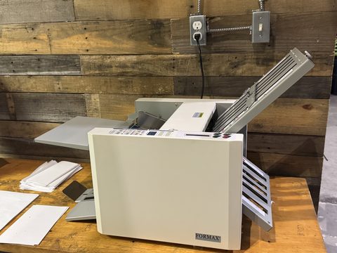 Formax paper folder on a wooden workbench against a wood plank wall
